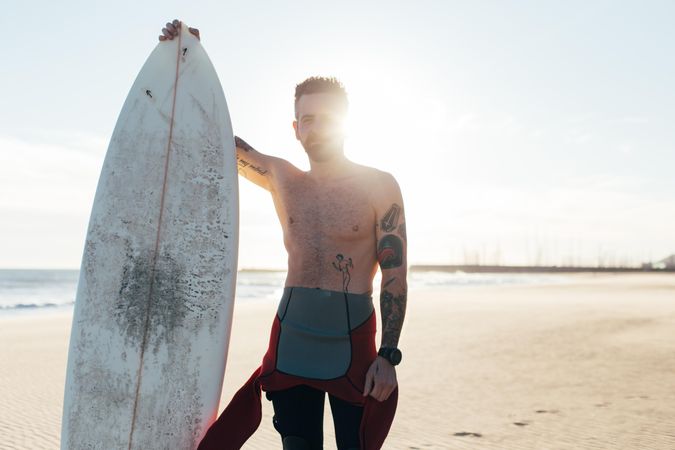 Medium shot of surfer in the sun in wetsuit with surfboard and copy space