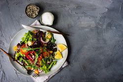 Top view of organic vegetable salad with side of salt and sesame seeds and space for text