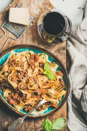 Pasta dinner with minced meat, cheese and red wine on wooden board