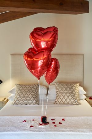 Hotel bedroom decorated with red heart balloons and rose petals