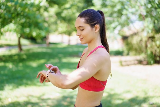 Active woman in the park uses a smartwatch to track her outdoor workout, focusing on fitness and performance monitoring