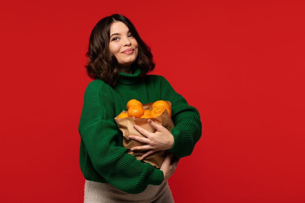 Woman in green sweater hugging bag full of ripe tangerines