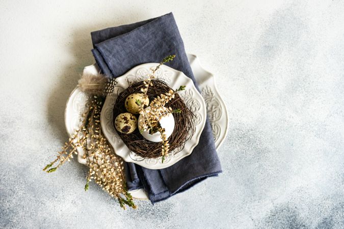 Top view of Easter table setting with decorative egg shell, feather and heather on grey counter with copy space