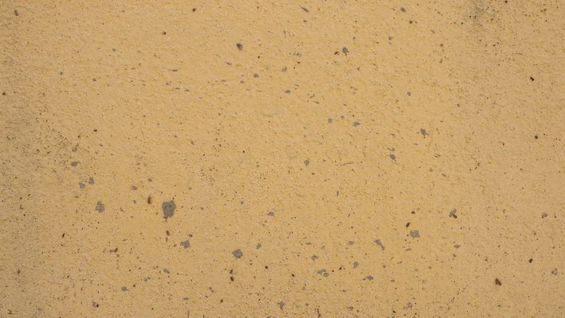 Pale yellow concrete wall with rough surface texture and small speckled details