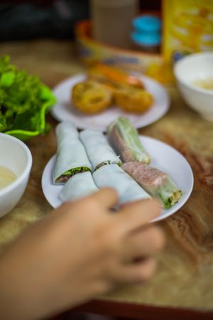 Cropped image of a hand beside vegetable rice rolls on plate on wooden table