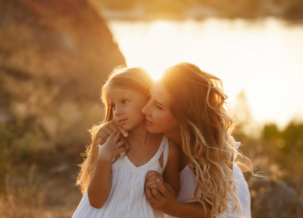 Woman leaning down behind daughter at dusk