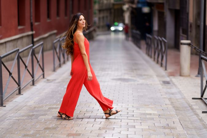 A Stylish Woman Dressed in a Bold Red Jumpsuit is Walking Alone in an Urban Setting