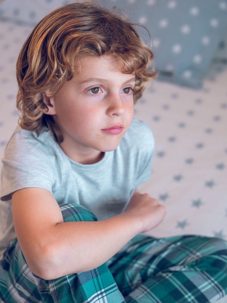 Adorable little boy sitting on bed and dreaming