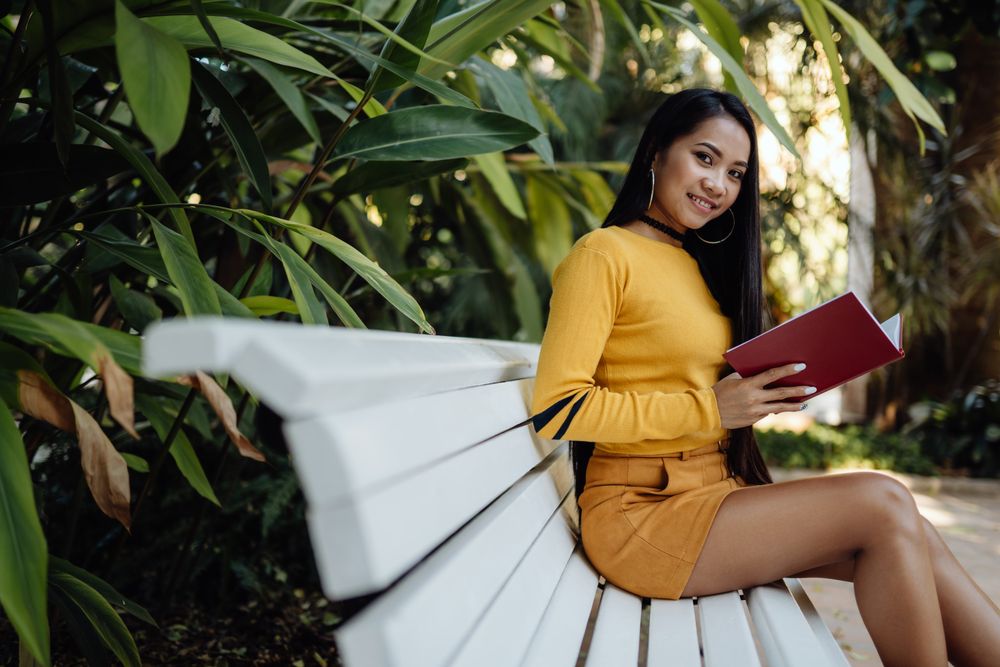 Graceful long haired Asian woman reading book on bench in park