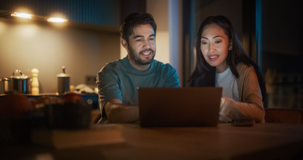 Portrait of Young Couple Using Laptop Computer While Sitting in the Kitchen at Home.