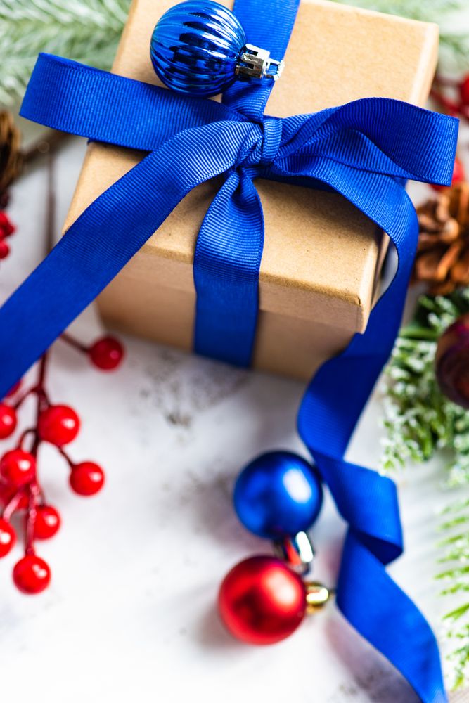 Top view of present wrapped in blue bow with holly, baubles and pine
