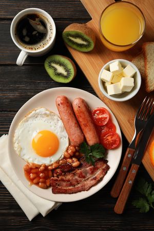 Wooden table with breakfast plate of eggs, tomatoes, sausage and bacon, vertical