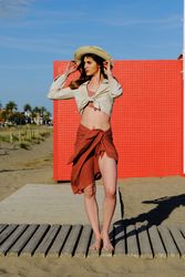 A long hair fashion model with a hat at the beach in front of a red wall