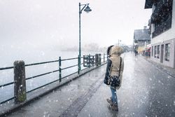 Woman walking near a lake during snowfall dressed in winter clothes