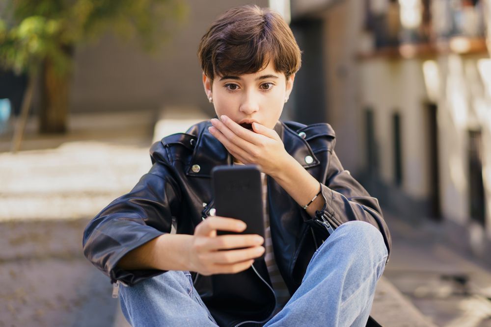 A surprised young individual engaging deeply with their smartphone while sitting on urban steps