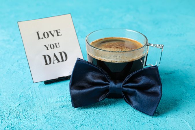 Blue bow tie, cup of coffee and inscription love you DAD on color background, space for text