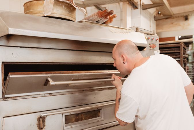 Bald baker checking pastry inside oven