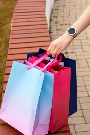 Shopper's hand grasping vibrant paper bags placed on bench.