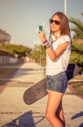 Young girl with skateboard and headphones looking smartphone