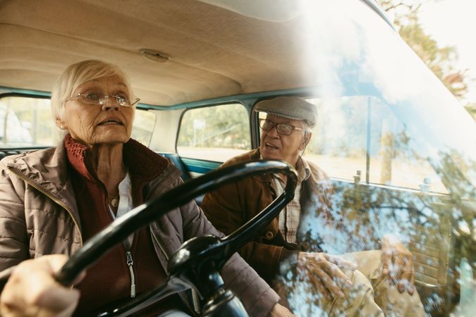 Mature woman driving a car with a man sitting in passenger seat looking at her