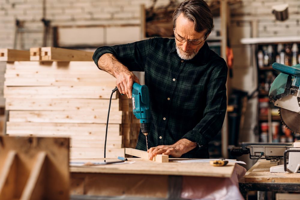 Carpenter using electric drill in woodworking studio