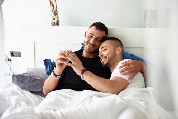 Smiling gay couple hugging on bed