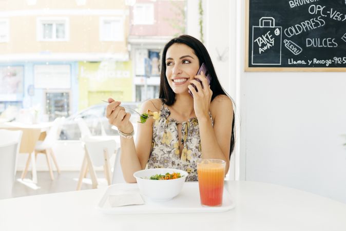 Cheerful woman with healthy food talking on smartphone in cafe
