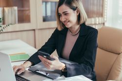 Woman smiling at phone while sitting in her office with laptop