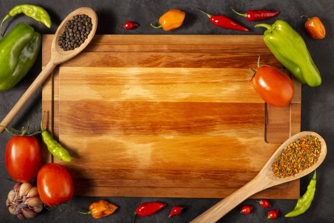 Empty cutting  board on the table with Ingredients for cooking. Tomatoes, various peppers, garlic and green peppers.