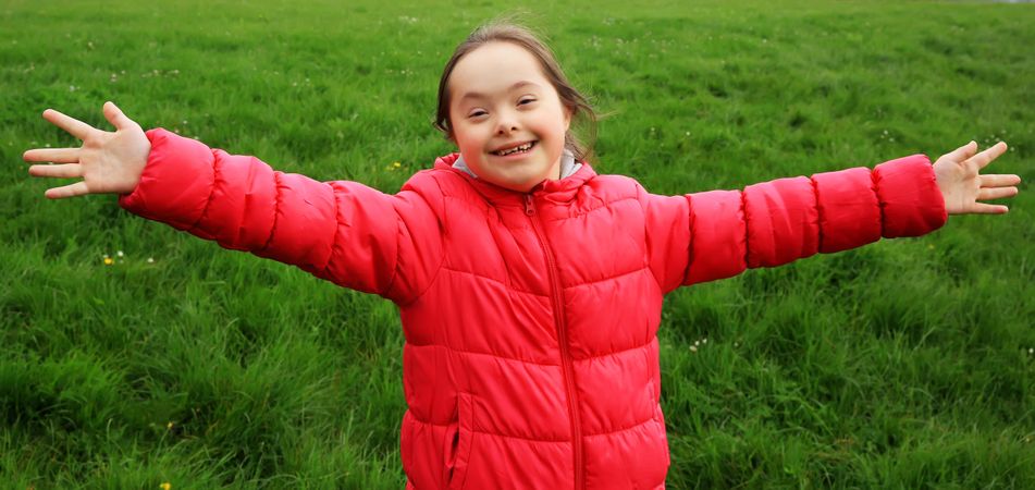 Portrait of girl with Down syndrome with outstretched arms in the park