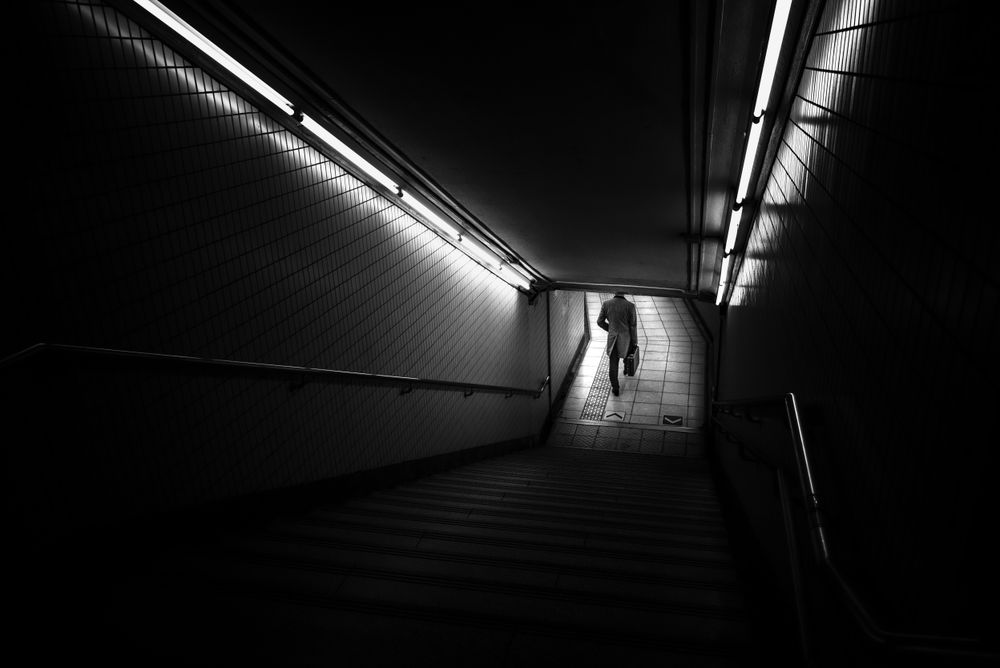 Grayscale photo of man walking outdoor of a building