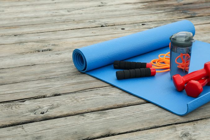 Yoga mat, jump rope, dumbbells and water bottle on wooden floor, space for text