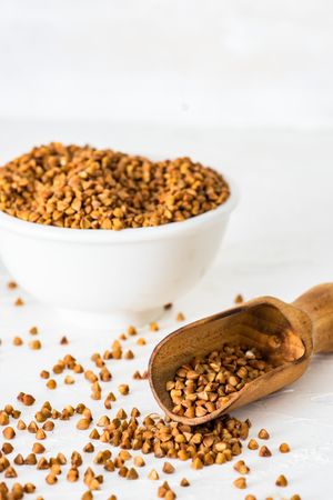 Organic raw buckwheat seeds in a bowl on wooden table with scoop