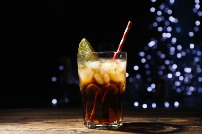 Glass with cola, lime slice and tubule against blurred lights background
