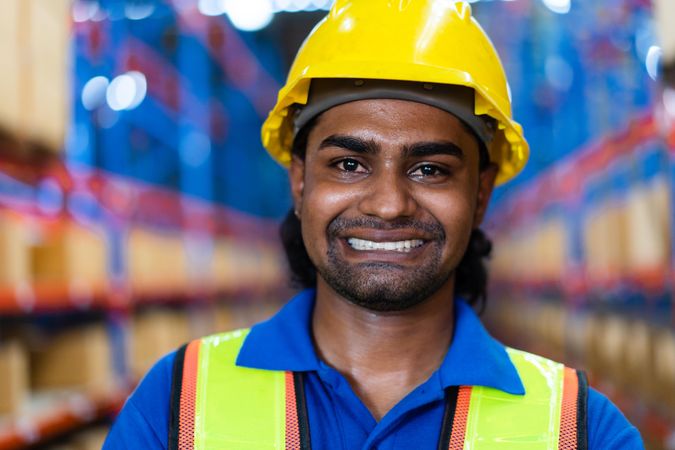 Smiling man in distribution center wearing hard hat and high visibility vest