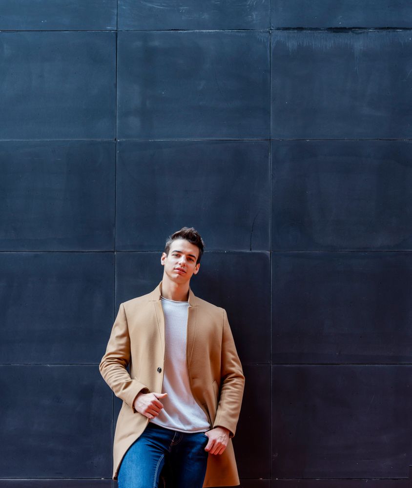 Cool young man in the center wearing winter coat looking at camera against dark wall