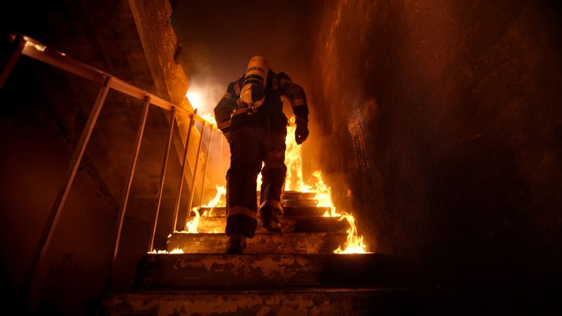 Strong and brave firefighter going up stairs in burning building