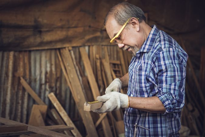 Mature Asian male carpenter measuring a wooden panel in workshop