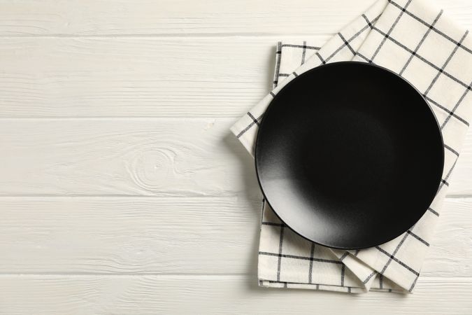 Kitchen towel with plate on wooden background, top view