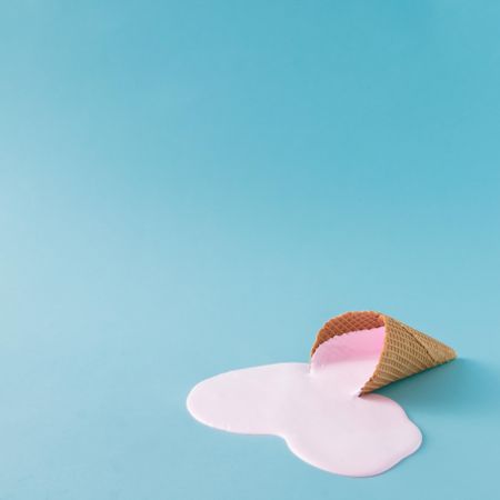 Melted pink ice cream and waffle cone on pastel blue background
