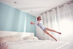 Joyful boy jumping on bed in morning