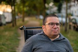Portrait of content man sitting in wheelchair in park path