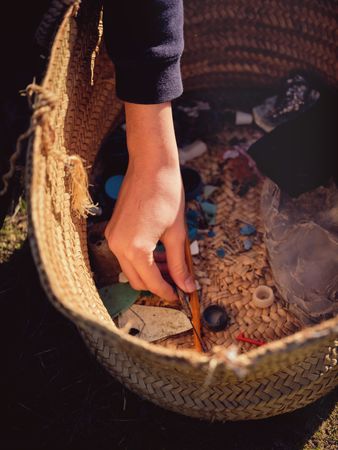 Crop person putting picked up piece of plastic into basket