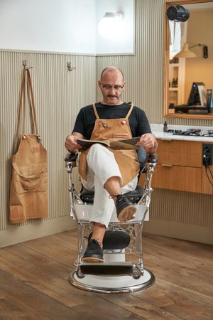 Confident barber sitting with magazine in barbershop