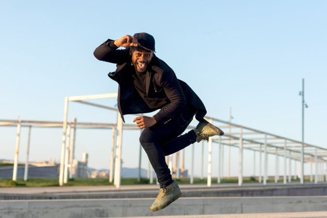 Smiling Black bearded man jumping and holding hat on a sunny day