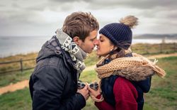 Couple kissing with coffee mugs on cliff above the ocean