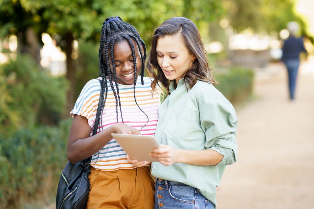Women friends pointing at something on tablet in casual clothing outside