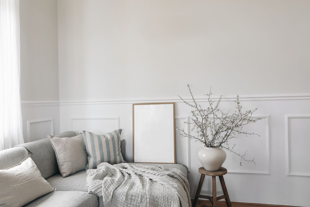 Stylish living room with vase, blooming cherry plum tree branches with mockup poster