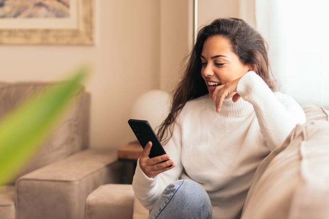 Connected at Home: Young Woman Sitting on Sofa Using Smartphone