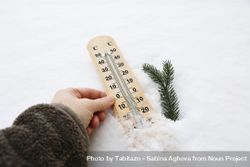 Closeup of womans hand in fleece sweatshirt holding thermometer showing a temperature in Celsius degrees below zero 4jP1X0